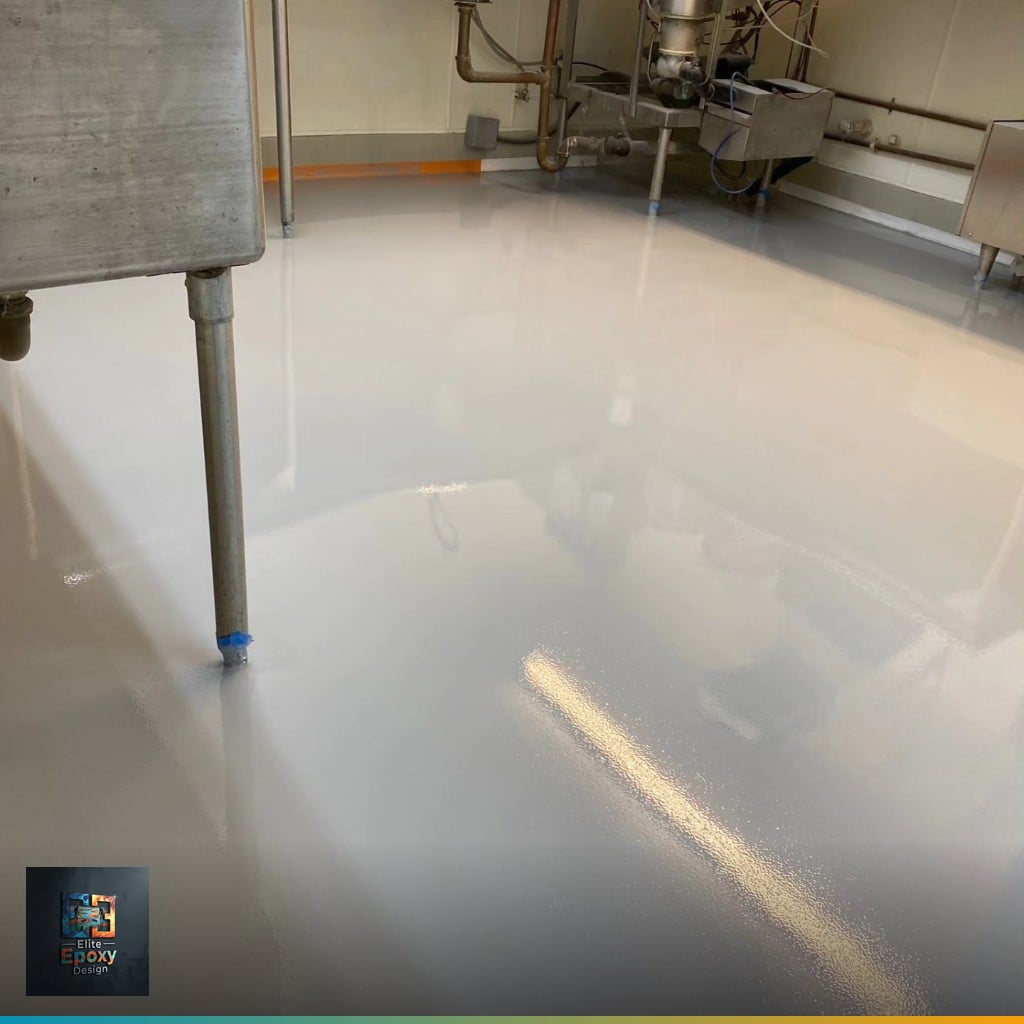 Seamless light gray resin floor in a commercial kitchen beneath stainless steel prep benches and pipework